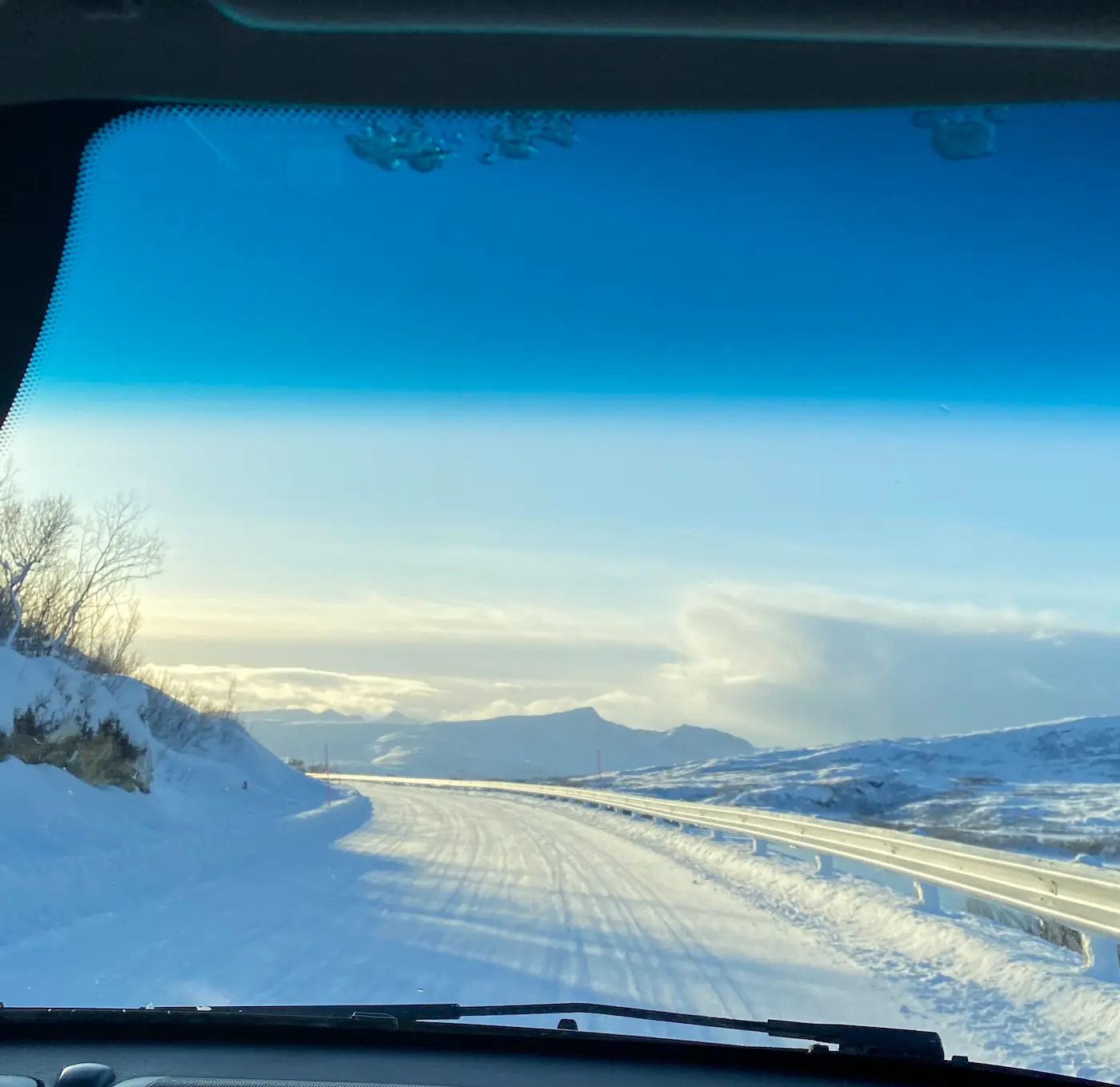 View through a car windshield of snowy roads and sunlit mountains on the way to Sommarøy.